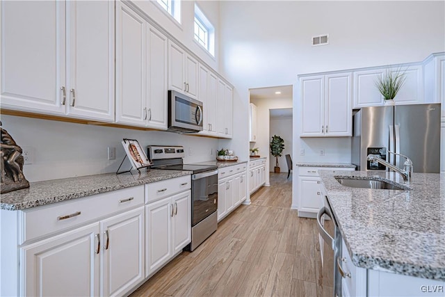 kitchen featuring light wood-type flooring, light stone counters, stainless steel appliances, sink, and white cabinets