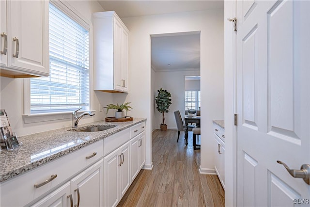 kitchen featuring light stone countertops, light hardwood / wood-style floors, white cabinetry, and sink