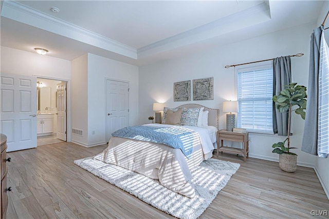 bedroom with ornamental molding, light hardwood / wood-style floors, ensuite bath, and a tray ceiling