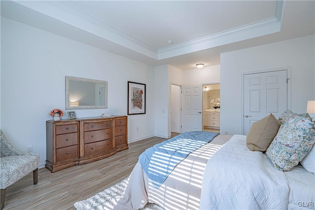 bedroom with ornamental molding, ensuite bathroom, a tray ceiling, and light hardwood / wood-style floors