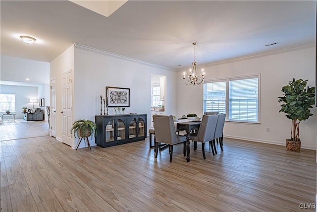 dining room with light wood-type flooring, ornamental molding, and an inviting chandelier