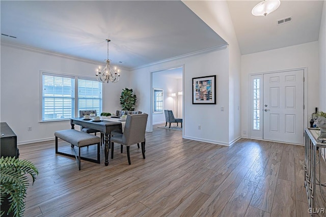 dining space featuring hardwood / wood-style floors, vaulted ceiling, an inviting chandelier, and ornamental molding