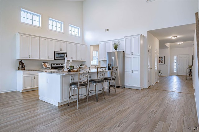 kitchen with light wood-type flooring, a towering ceiling, appliances with stainless steel finishes, a kitchen island, and white cabinetry