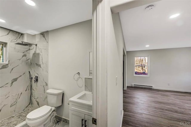 bathroom featuring a tile shower, vanity, a baseboard heating unit, hardwood / wood-style flooring, and toilet