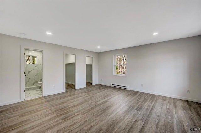 unfurnished bedroom with ensuite bath, a walk in closet, a baseboard radiator, and light hardwood / wood-style floors