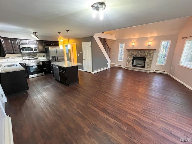 kitchen with a center island, a baseboard radiator, a stone fireplace, pendant lighting, and appliances with stainless steel finishes