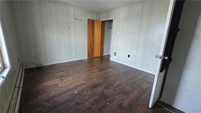 empty room featuring dark hardwood / wood-style flooring, a baseboard radiator, and wooden walls