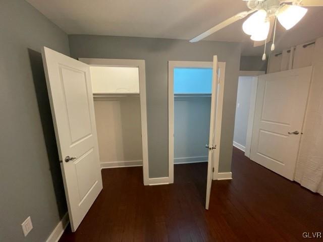 unfurnished bedroom featuring ceiling fan, a closet, dark wood-type flooring, and a spacious closet