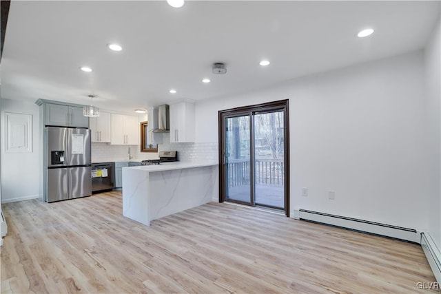 kitchen with kitchen peninsula, appliances with stainless steel finishes, wall chimney exhaust hood, baseboard heating, and hanging light fixtures