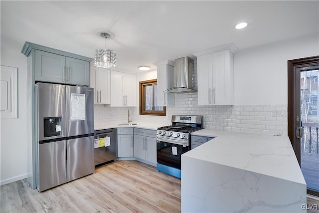 kitchen with appliances with stainless steel finishes, light wood-type flooring, wall chimney range hood, pendant lighting, and white cabinets