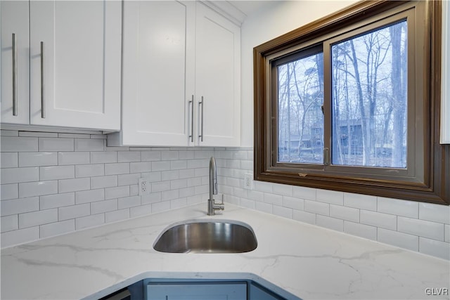 interior details featuring light stone counters, white cabinetry, and sink