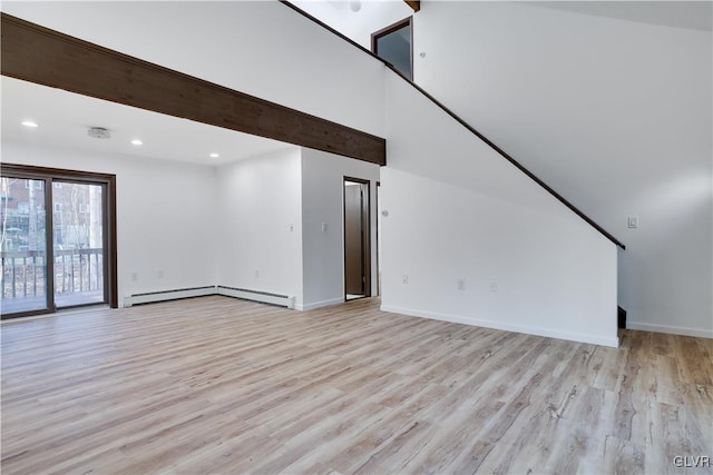 unfurnished living room with a towering ceiling, light hardwood / wood-style flooring, and a baseboard heating unit