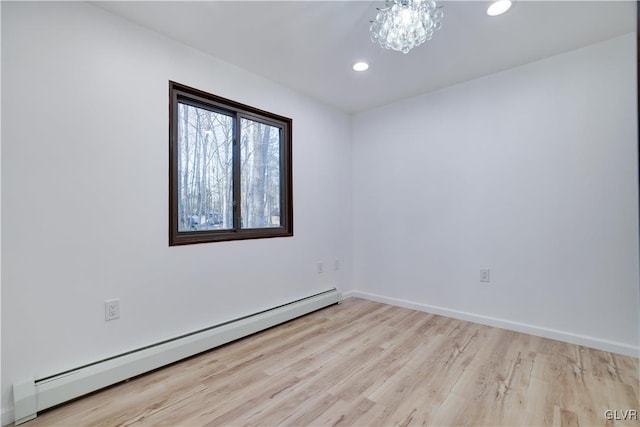 empty room featuring light hardwood / wood-style flooring, an inviting chandelier, and a baseboard heating unit