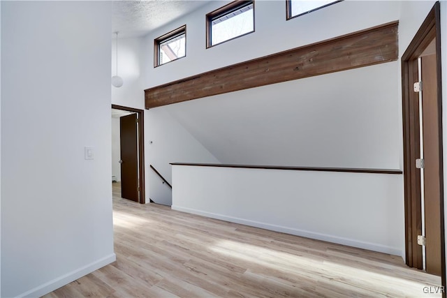 empty room with a textured ceiling, light hardwood / wood-style floors, and vaulted ceiling