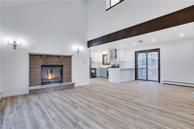 unfurnished living room with beam ceiling, light wood-type flooring, baseboard heating, and a brick fireplace