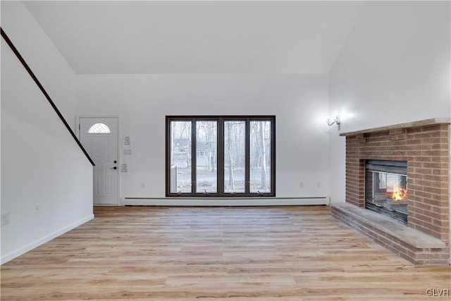 unfurnished living room featuring baseboard heating, a fireplace, vaulted ceiling, and light wood-type flooring