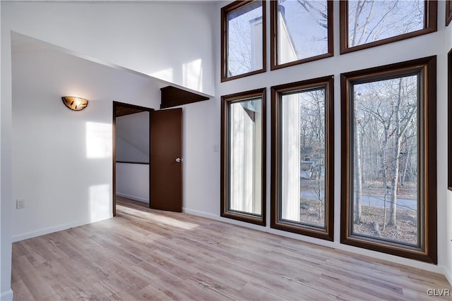 unfurnished room featuring plenty of natural light, light hardwood / wood-style floors, and a high ceiling