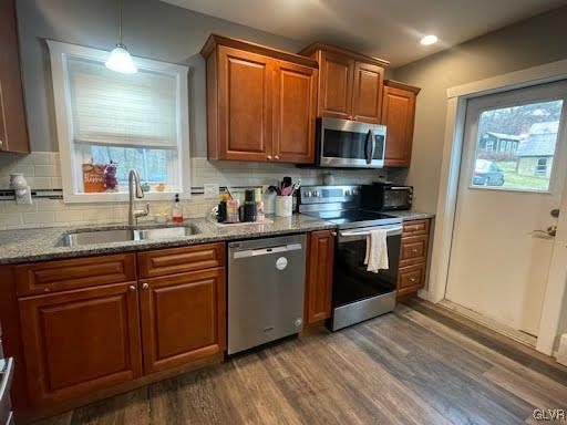 kitchen featuring sink, stainless steel appliances, light stone counters, dark hardwood / wood-style floors, and decorative backsplash