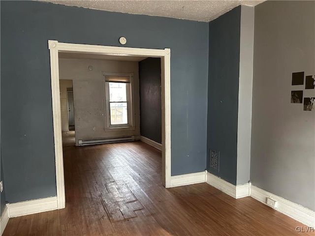 empty room featuring baseboard heating, wood-type flooring, and a textured ceiling