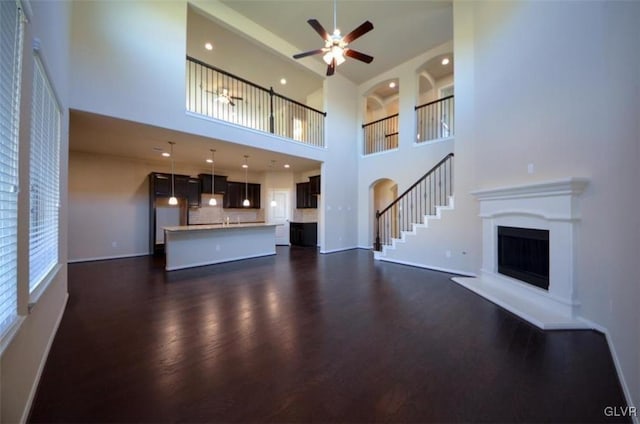 unfurnished living room with ceiling fan, dark hardwood / wood-style flooring, and a high ceiling