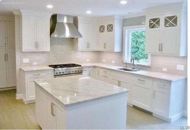 kitchen with a center island, wall chimney range hood, sink, high end stove, and white cabinetry