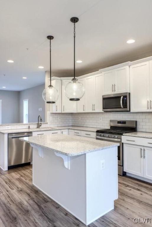 kitchen featuring appliances with stainless steel finishes, light hardwood / wood-style flooring, a center island, white cabinetry, and hanging light fixtures