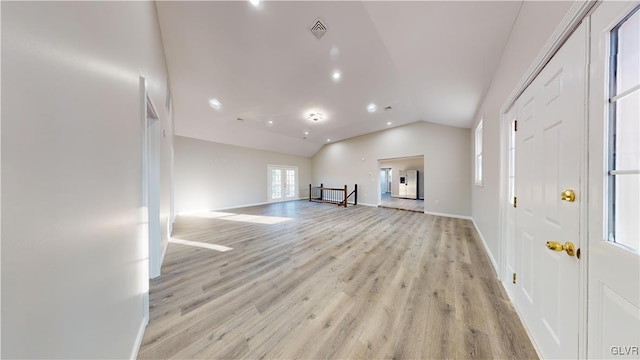 unfurnished living room with a wealth of natural light, vaulted ceiling, and light wood-type flooring