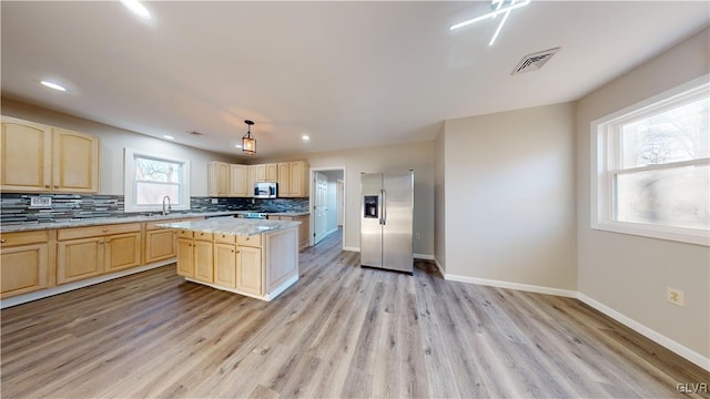 kitchen featuring decorative backsplash, light brown cabinetry, light wood-type flooring, stainless steel appliances, and a center island