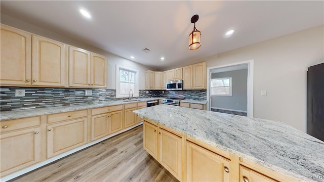 kitchen with appliances with stainless steel finishes, light stone counters, light brown cabinets, decorative light fixtures, and light hardwood / wood-style flooring