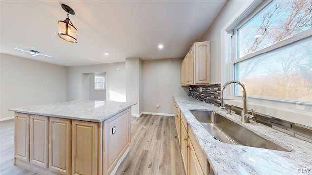 kitchen featuring decorative backsplash, light stone countertops, sink, light brown cabinets, and pendant lighting