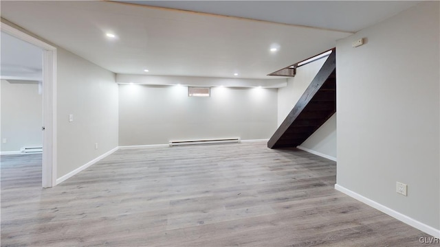 basement featuring light wood-type flooring and a baseboard heating unit