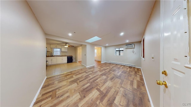 unfurnished living room featuring a skylight, sink, light hardwood / wood-style flooring, a baseboard heating unit, and an AC wall unit