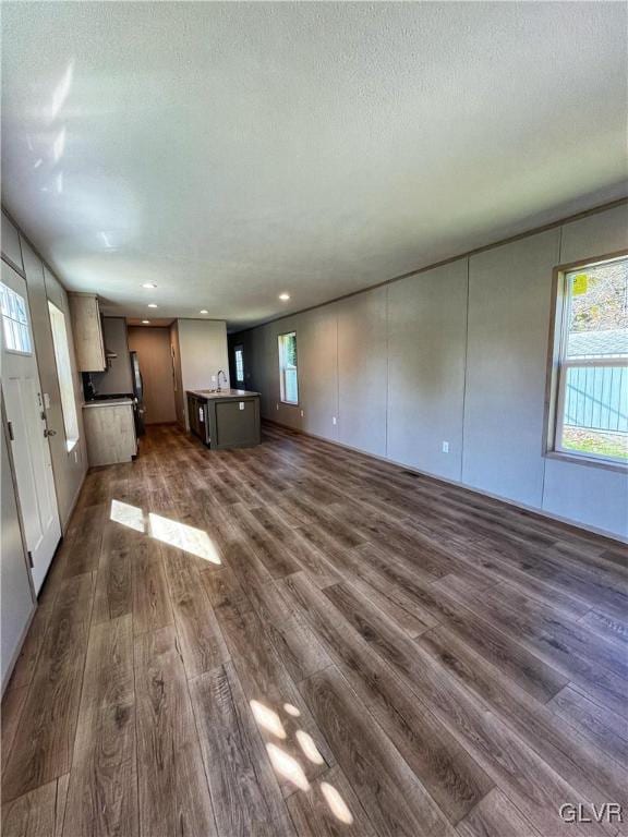 unfurnished living room featuring a healthy amount of sunlight, sink, and dark wood-type flooring