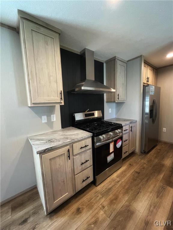 kitchen featuring hardwood / wood-style flooring, light stone countertops, wall chimney range hood, and appliances with stainless steel finishes