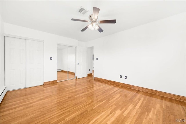 unfurnished bedroom featuring hardwood / wood-style floors, ceiling fan, a baseboard heating unit, and multiple closets