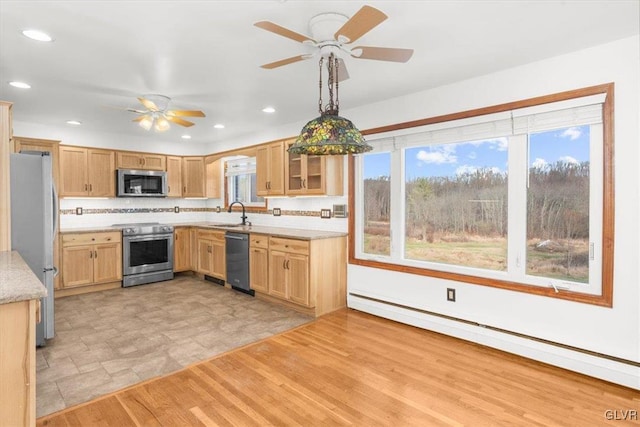 kitchen with a baseboard heating unit, sink, hanging light fixtures, light wood-type flooring, and stainless steel appliances