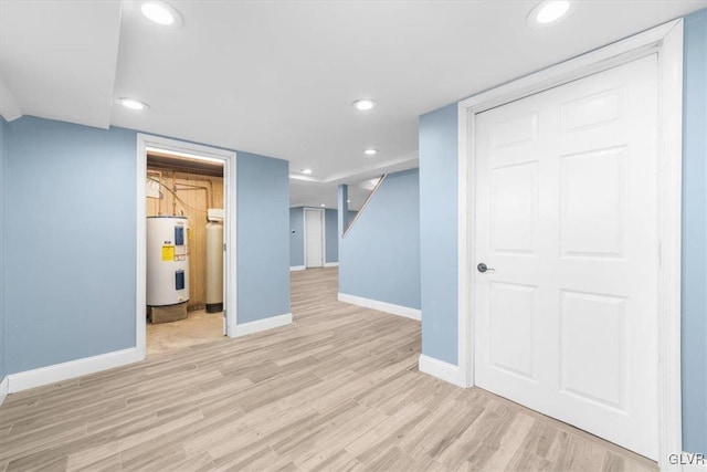 basement with light hardwood / wood-style flooring and water heater