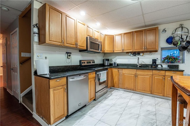 kitchen with a drop ceiling, dark stone countertops, sink, and stainless steel appliances