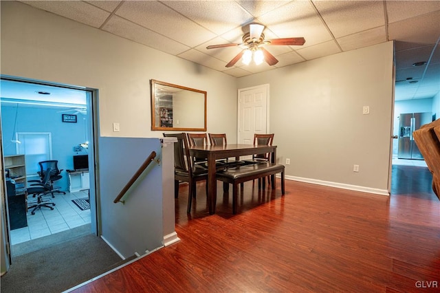 dining room featuring dark hardwood / wood-style flooring, a drop ceiling, and ceiling fan