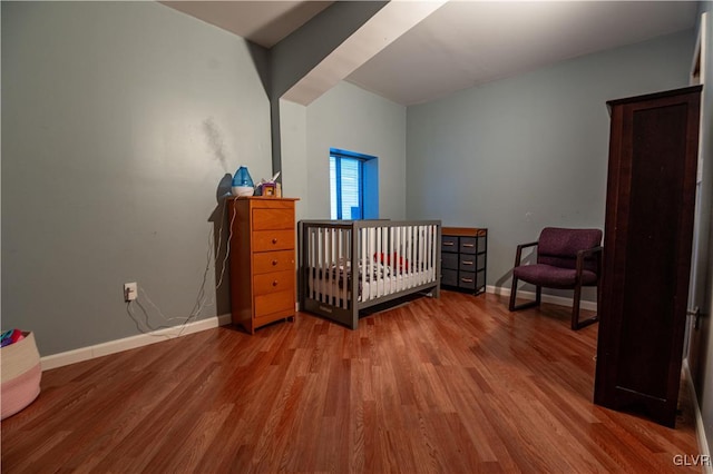 bedroom with wood-type flooring and a nursery area