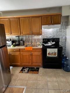 kitchen featuring exhaust hood, decorative backsplash, light tile patterned floors, black / electric stove, and stainless steel refrigerator