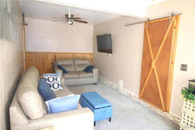 carpeted living room featuring a barn door, ceiling fan, and wood walls