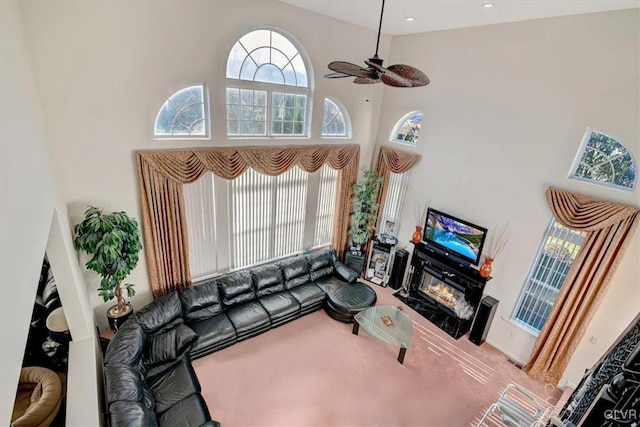 living room with ceiling fan, a fireplace, carpet, and a high ceiling