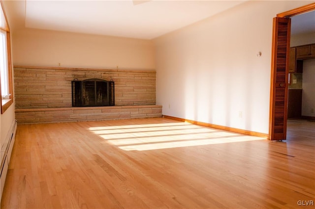 unfurnished living room featuring light wood-type flooring, a stone fireplace, and a baseboard heating unit