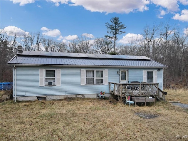 rear view of property featuring a yard, a deck, and solar panels