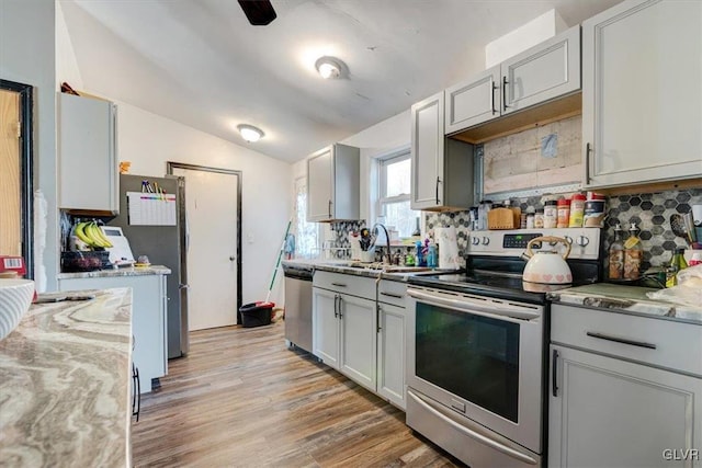 kitchen with light stone countertops, backsplash, light hardwood / wood-style floors, lofted ceiling, and appliances with stainless steel finishes