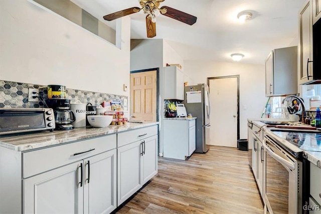 kitchen featuring light stone countertops, ceiling fan, sink, light hardwood / wood-style floors, and appliances with stainless steel finishes