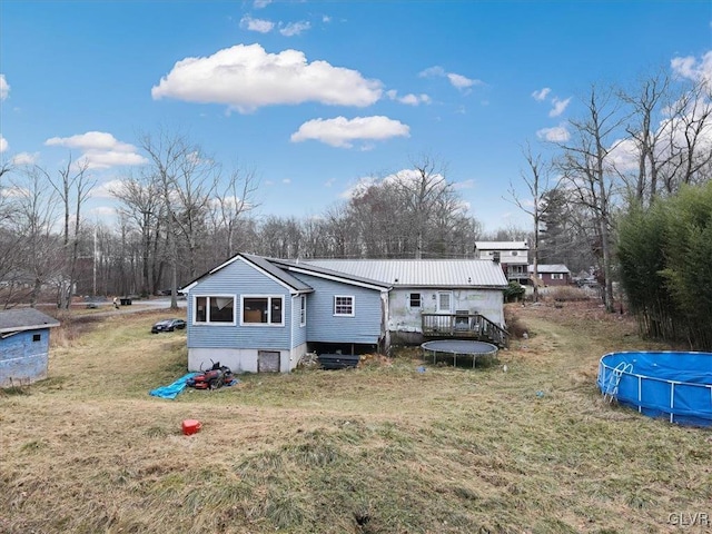 back of house featuring a trampoline, a pool side deck, and a lawn