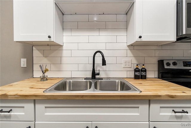 kitchen featuring butcher block countertops, sink, white cabinetry, and backsplash