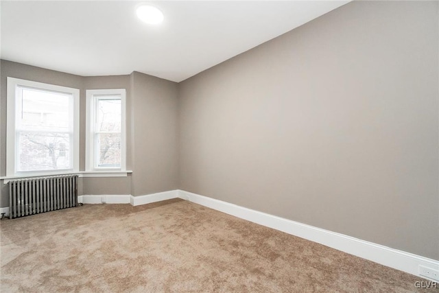 spare room featuring light colored carpet and radiator